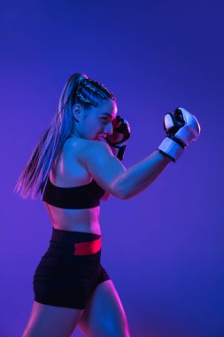 Atletik bayan MMA dövüşçüleri mavi-pembe arka planda neon ışıkta eğitiliyor.