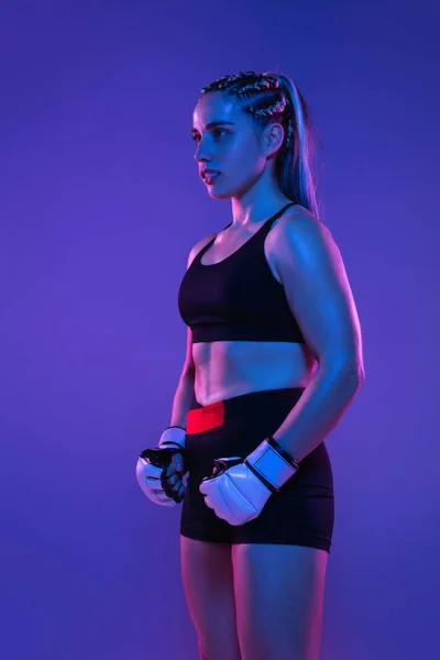 Athletic female MMA fighter posing isolated on blue background in neon light