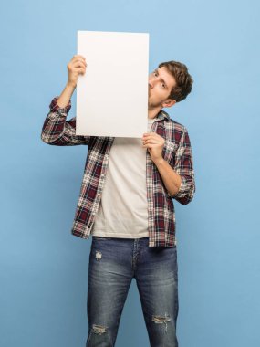 Mavi arka planda izole edilmiş tabelalı genç adam portresi.