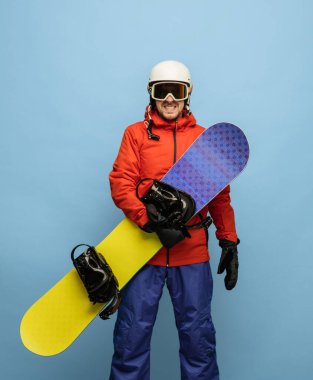 Mavi arka planda kayak takımlı genç snowboardcu izole edildi..