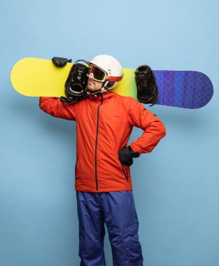 Mavi arka planda parlak kayak takımı ve snowboard giyen genç adam izole edilmiş..