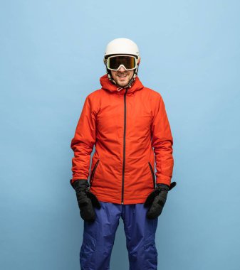 Parlak kayak takımı, kask ve gözlük takan atletik adam mavi arka planda izole edilmiş..