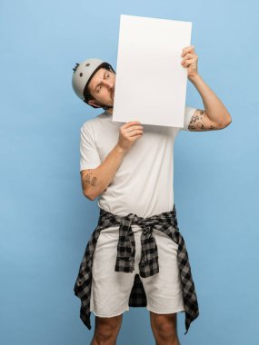 Mavi arka planda, boş bir kağıt parçasıyla şok olmuş genç bir adam.