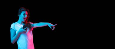 Akıllı telefonlu genç ve güzel bir kız karanlık arka planda neon ışıkta izole edilmiş.