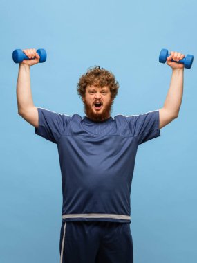 Mavi spor üniformalı komik kızıl saçlı adam mavi arka planda izole edilmiş.