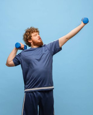 Mavi spor üniformalı komik kızıl saçlı adam mavi arka planda izole edilmiş.