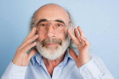 Yakın plan yaşlı gri saçlı gözlüklü adam açık mavi arka planda izole edilmiş..