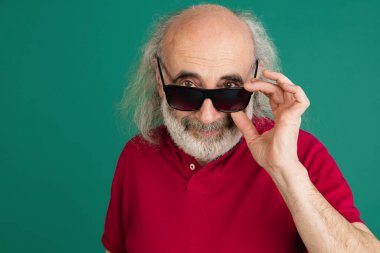 Yakın plan, yeşil arka planda izole edilmiş güneş gözlüklü gri saçlı yaşlı adam..
