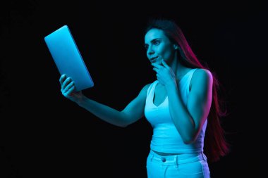 Tablet kullanan güzel bir kız. Karanlık arka planda, neon ışıkta izole edilmiş.