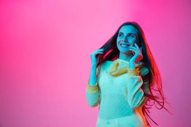 Telefonda konuşan güzel bir kız. Pembe arka planda, neon ışıkta izole edilmiş.