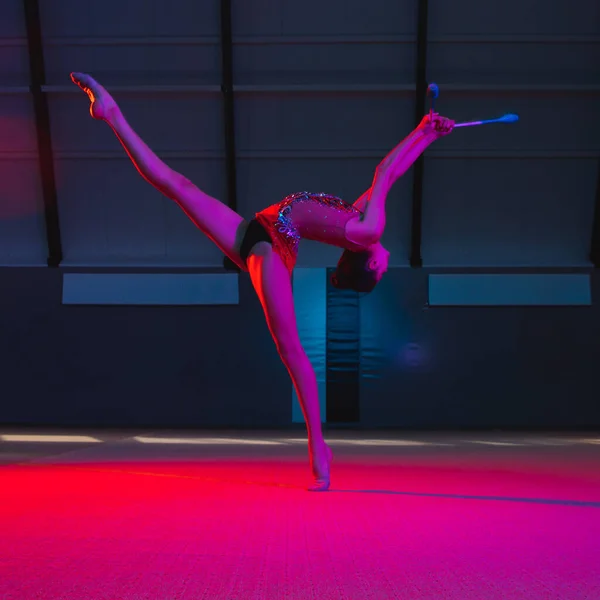 Young female rhythmic gymnast isolated on multicolored background in neon light