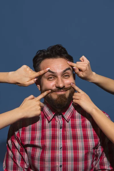 Mavi arka planda genç sakallı, yakışıklı adamı gülümseten kadın elleri.