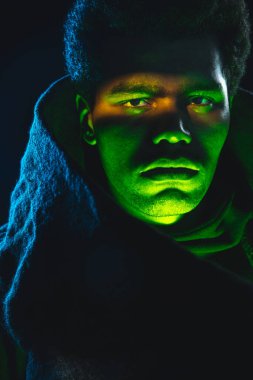 Siyah arka planda neon ışıkta izole edilmiş Afro-Amerikalı genç bir adam portresi.