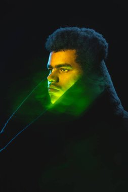 Siyah paltolu Afro-Amerikalı bir gencin portresi koyu arka planda izole edilmiş.