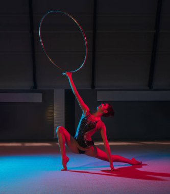 Genç zarif kız ritmik jimnastikçi, karanlık arka planda, neon ışığıyla izole edilmiş.