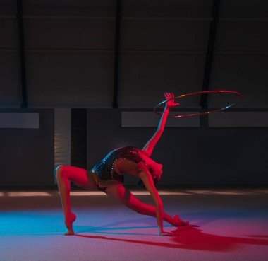 Genç zarif kız ritmik jimnastikçi, karanlık arka planda, neon ışığıyla izole edilmiş.