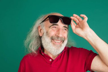 Yakın plan, yeşil arka planda izole edilmiş güneş gözlüklü gri saçlı yaşlı adam..