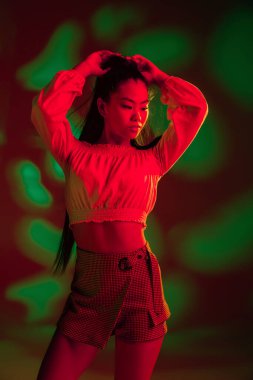Genç, güzel Asyalı kız kırmızı yeşil ışıklı arka planda yalnız poz veriyor..
