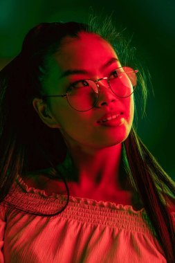 Genç, güzel Asyalı kız, kırmızı yeşil ışıklı arka planda izole edilmiş..