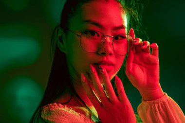 Genç, güzel Asyalı kız, kırmızı yeşil ışıklı arka planda izole edilmiş..