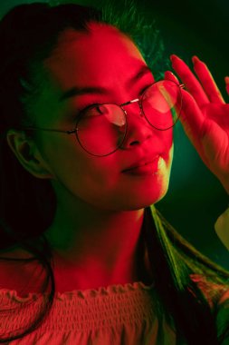 Genç, güzel Asyalı kız, kırmızı yeşil ışıklı arka planda izole edilmiş..