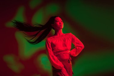 Genç, güzel Asyalı kız kırmızı yeşil ışıklı arka planda yalnız poz veriyor..