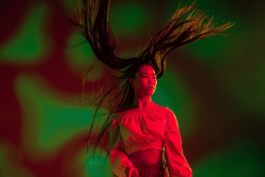 Genç, güzel Asyalı kız kırmızı yeşil ışıklı arka planda yalnız poz veriyor..