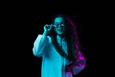 Güneş gözlüklü genç bir kız, karanlık arka planda, neon ışıkta izole edilmiş.