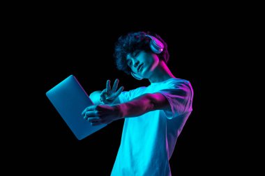 Tablet kullanan genç bir adamın portresi neon ışıkta koyu arkaplanda izole edilmiş.