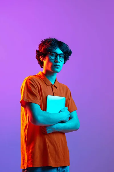 Young man in glasses with device isolated on gradient background in neon