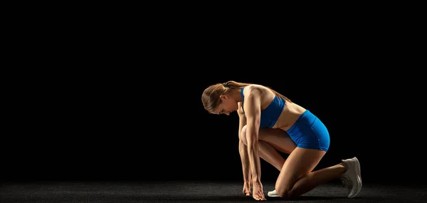 Young woman, track athlete training isolated over black studio background.
