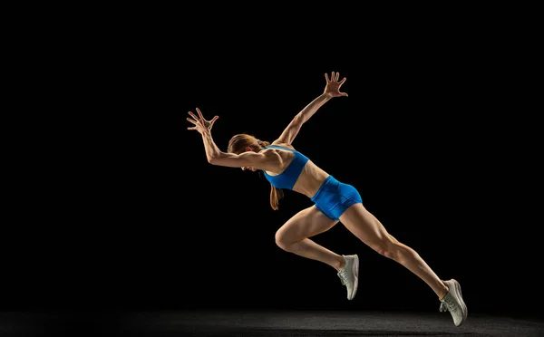 Sportive woman, track athlete training isolated over black studio background.
