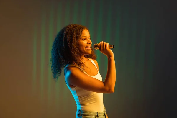 Young happy African-American girl isolated on colored background in neon. — Stock Photo, Image