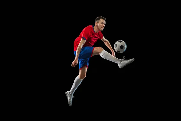 Young Caucasian soccer football player practicing isolated on black background. — Stock Photo, Image