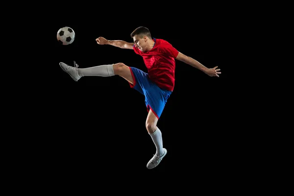 Junger kaukasischer Fußballspieler übt isoliert auf schwarzem Hintergrund. — Stockfoto