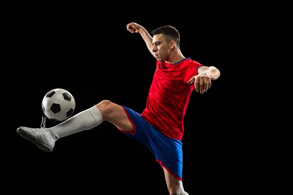 Giovane giocatore di calcio caucasico praticare isolato su sfondo nero. — Foto Stock
