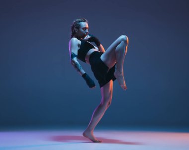 Genç bayan MMA dövüşçüsü mavi arka planda, neon ışıkta yalnız poz veriyor.