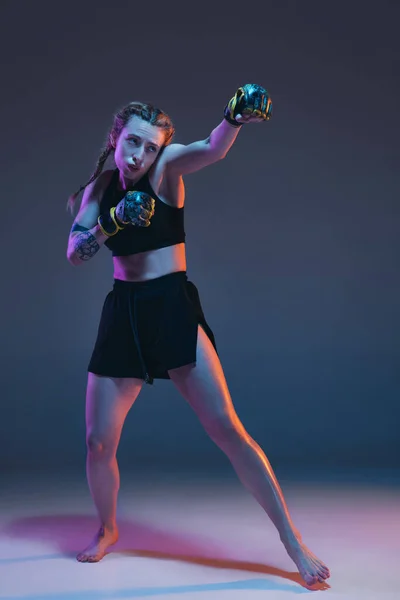 Young female MMA fighter training isolated over blue background in neon light — Stock Photo, Image