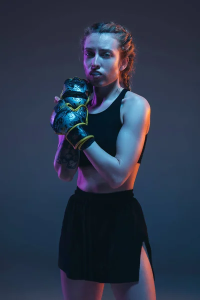 Caucasian female MMA fighter posing isolated over blue background in neon light