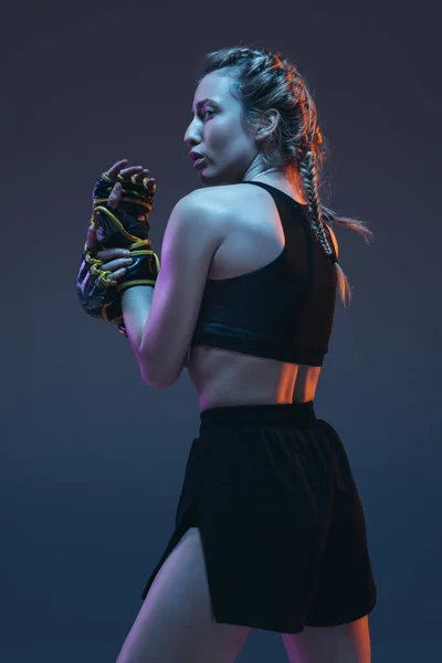 Caucasian female MMA fighter posing isolated over blue background in neon light