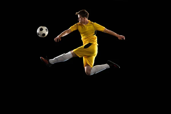 Ung man, manlig fotboll spelare träning isolerad på svart bakgrund. — Stockfoto