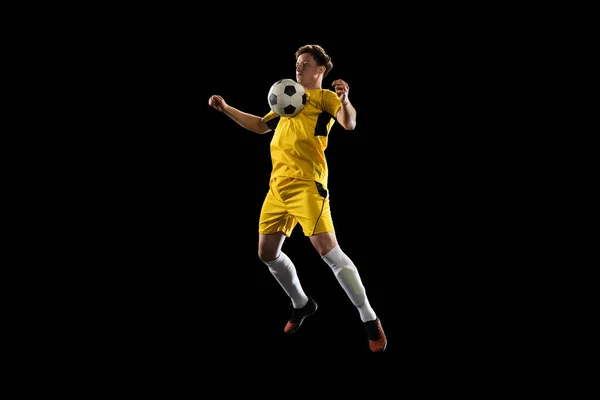 Jovem, jogador de futebol masculino treinando isolado em fundo preto. — Fotografia de Stock