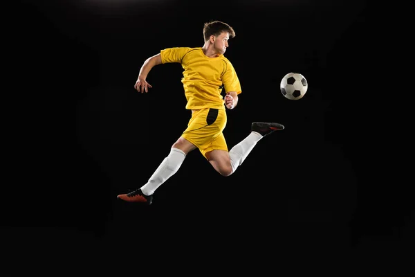 Jovem, jogador de futebol masculino treinando isolado em fundo preto. — Fotografia de Stock