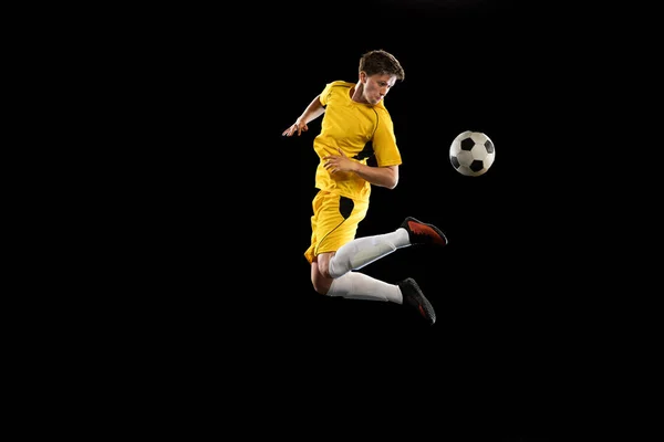 Jovem, jogador de futebol masculino treinando isolado em fundo preto. — Fotografia de Stock