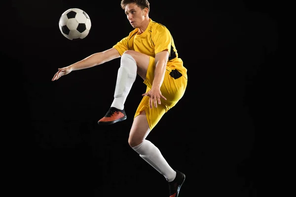 Jongeman, mannelijke voetbal speler training geïsoleerd op zwarte achtergrond. — Stockfoto