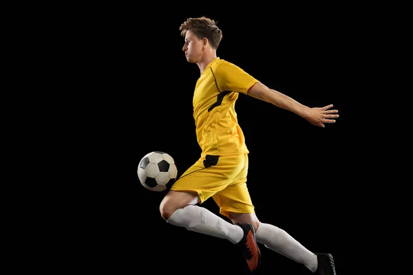 Un giocatore di calcio maschio che gioca a calcio isolato su sfondo nero. — Foto Stock