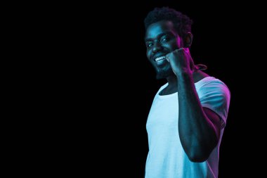 Mutlu gülümseyen Afro-Amerikalı adam, karanlık arka planda, neon ışıkta izole edilmiş.