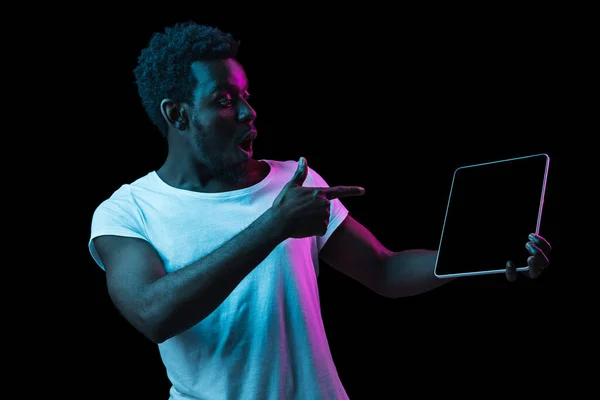 Young African-American man pointing to tablet screen in neon light. — Zdjęcie stockowe