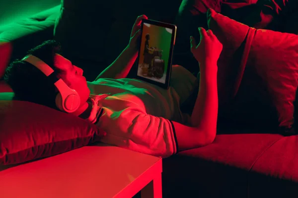 Young Korean man using tablet at home interior in gradient red green neon light