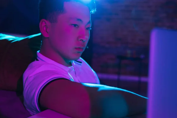 Close-up young Korean man isolated at home interior in gradient blue neon light — Stock Photo, Image